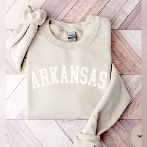 neutral crewneck sweatshirt features an arched collegiate-style "ARKANSAS"